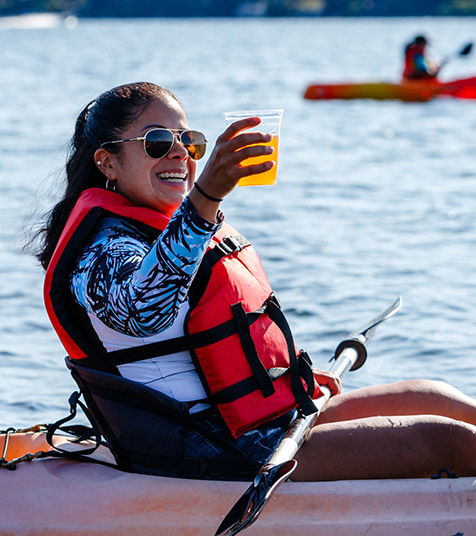 smiling woman kayaking with a beer in hand